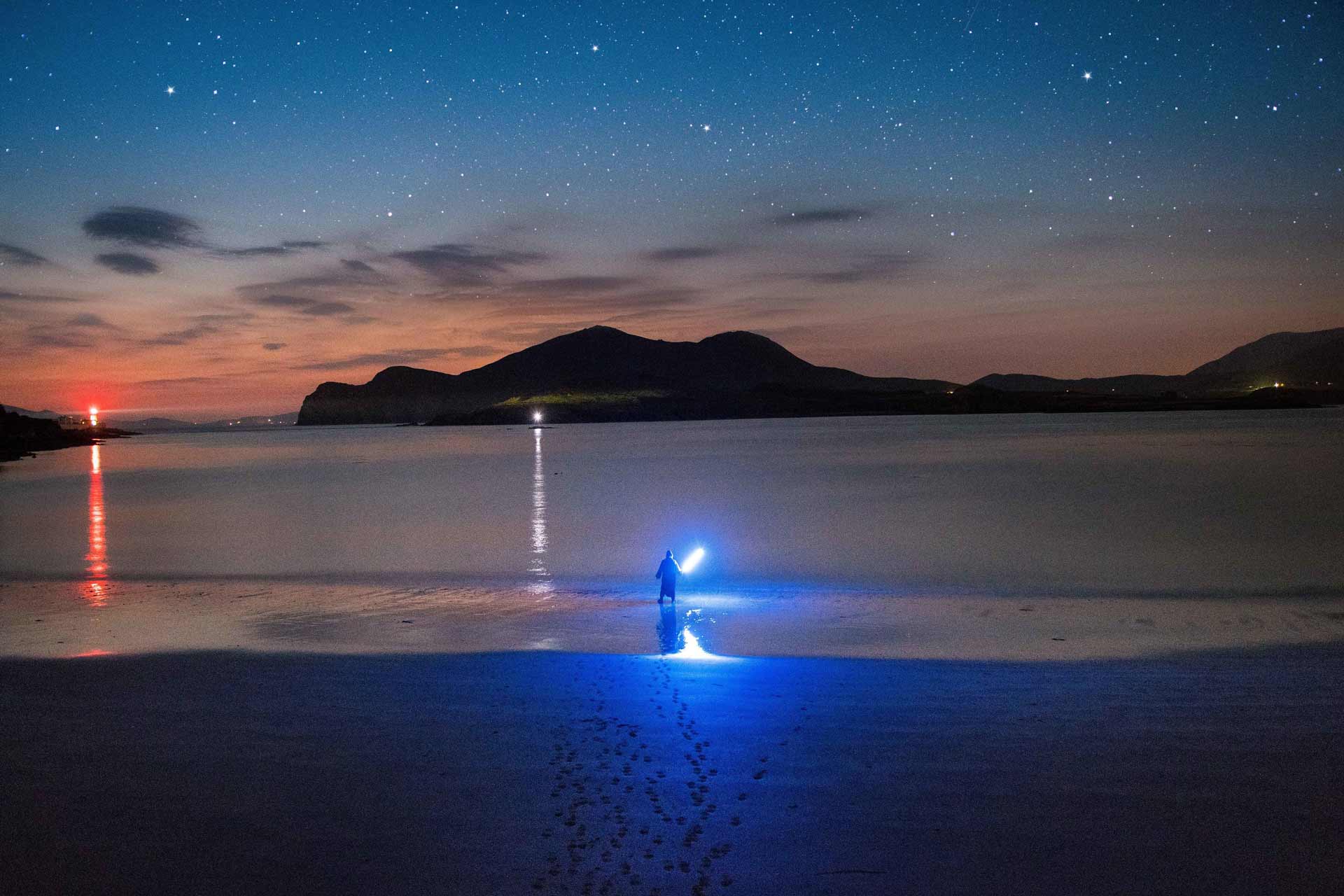 A lone man on the beach with a lightsaber under the starry night sky