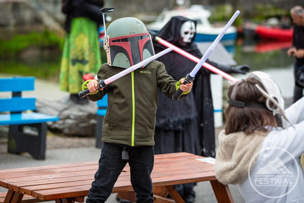A child with a boba fett helmet and two lightsabers