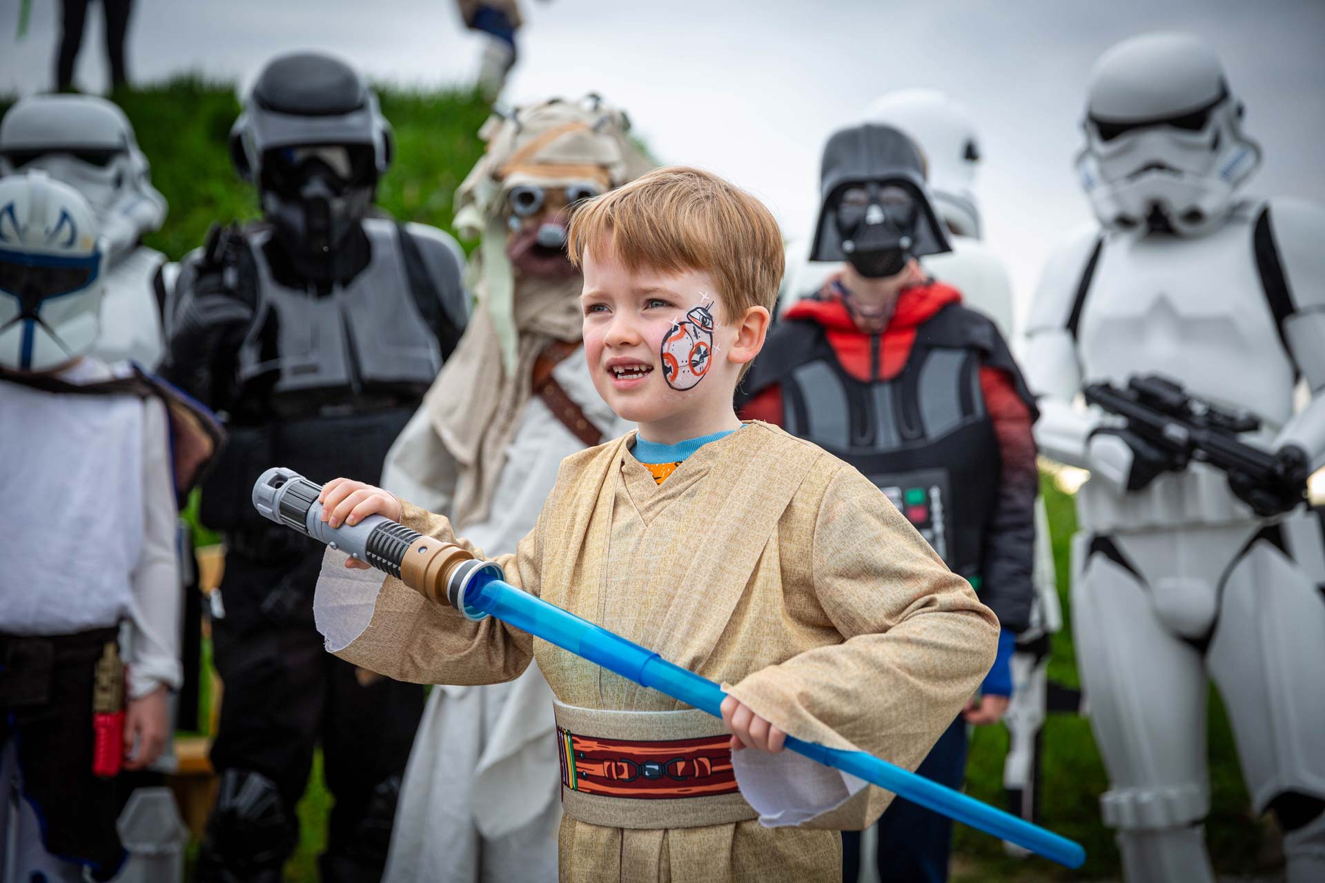 A young child with a blue lightsaber and facepaint